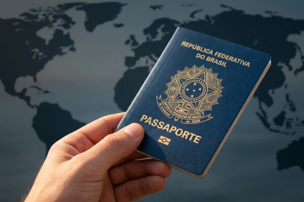 Mão segurando o passaporte brasileiro aberto em destaque com um mapa-múndi ao fundo, ilustrando viagens internacionais sem visto.